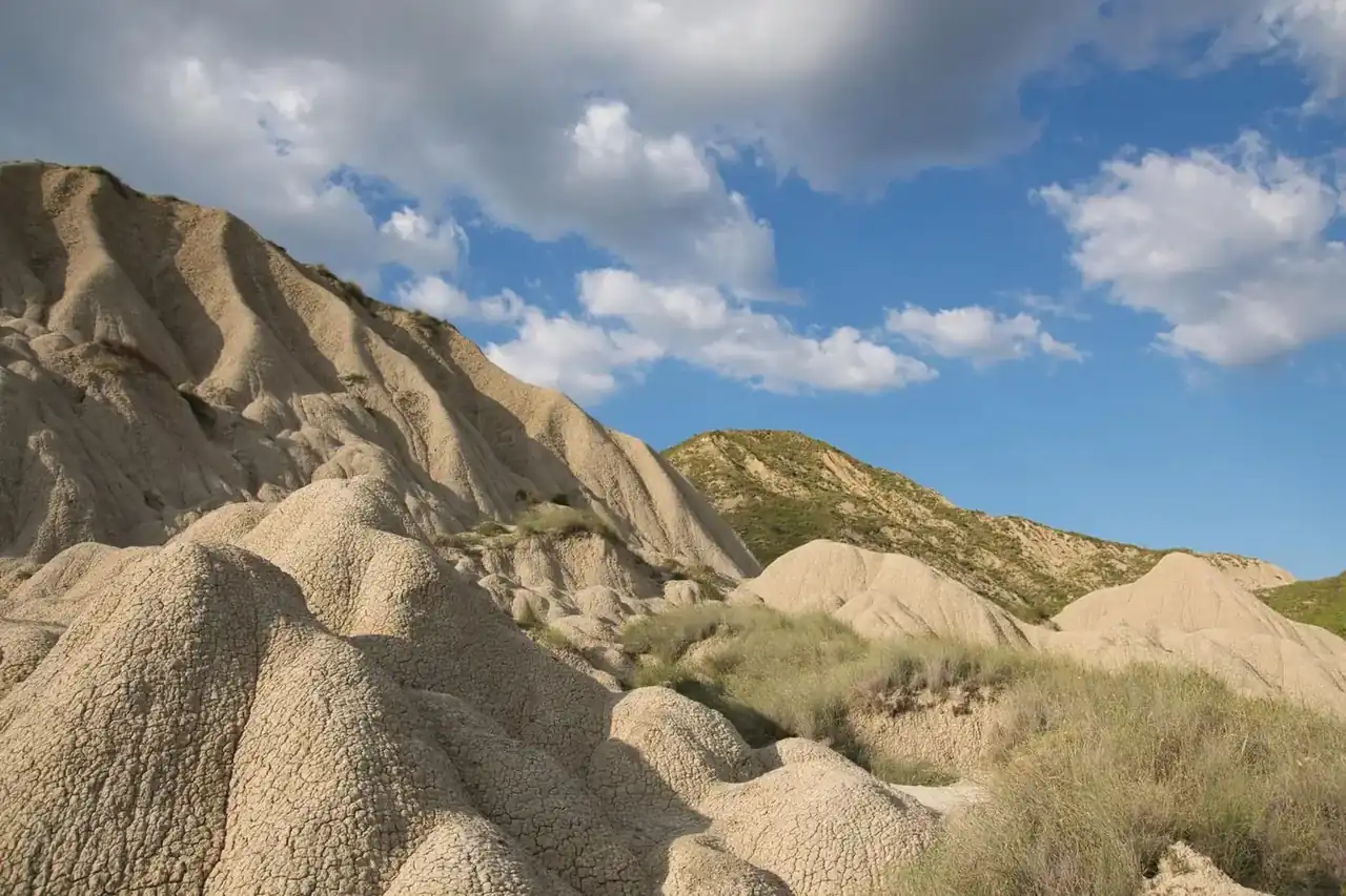 Clay badlands of Aliano, cracked clay ridges and grass under a blue sky with clouds