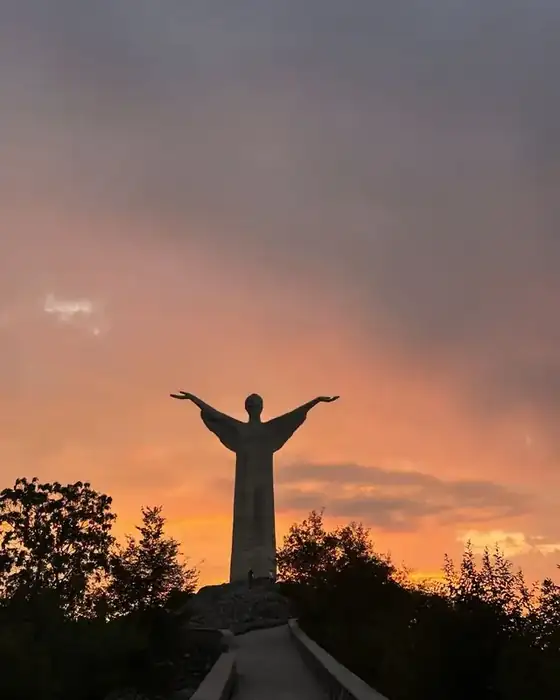 The Christ the Redeemer statue of Maratea in silhouette against an orange sunset sky