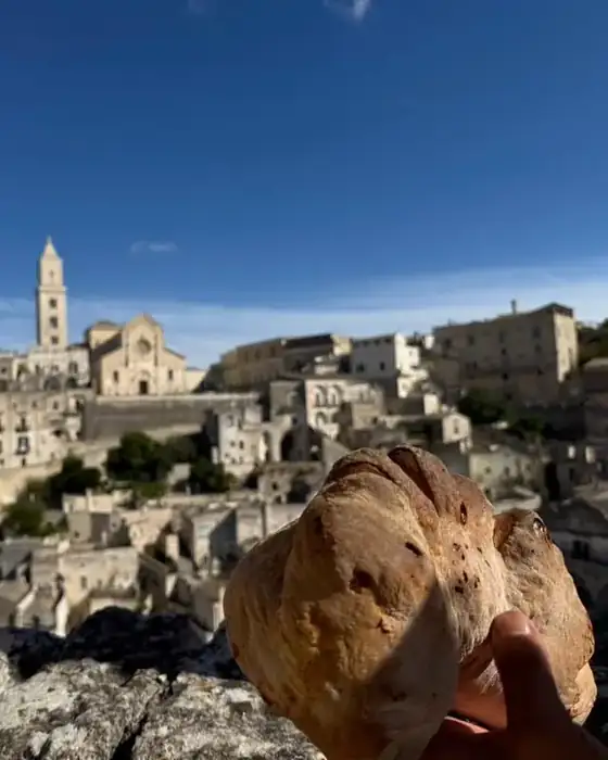 The Sassi of Matera and the cathedral bell tower under a deep blue sky, with a loaf of bread in the foreground