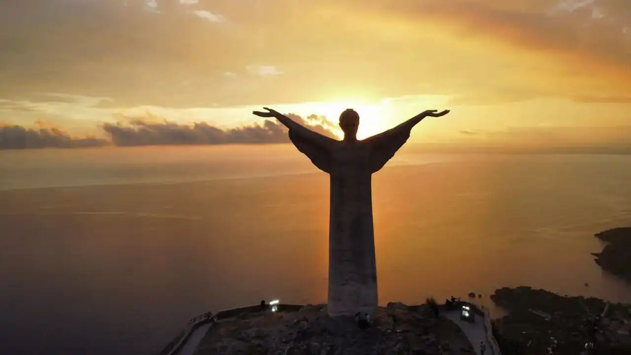 The Christ the Redeemer statue of Maratea with open arms, in silhouette against the setting sun over the sea